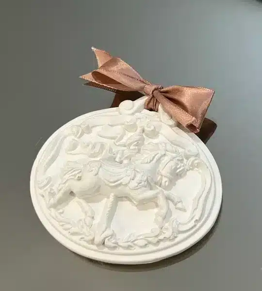 Medalhão decorativo em relevo com cavalos de carrossel e laço acetinado castanho.